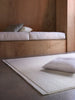 Città Joni Wool Mat in Oatmeal, styled beside a built-in bench on a concrete floor.