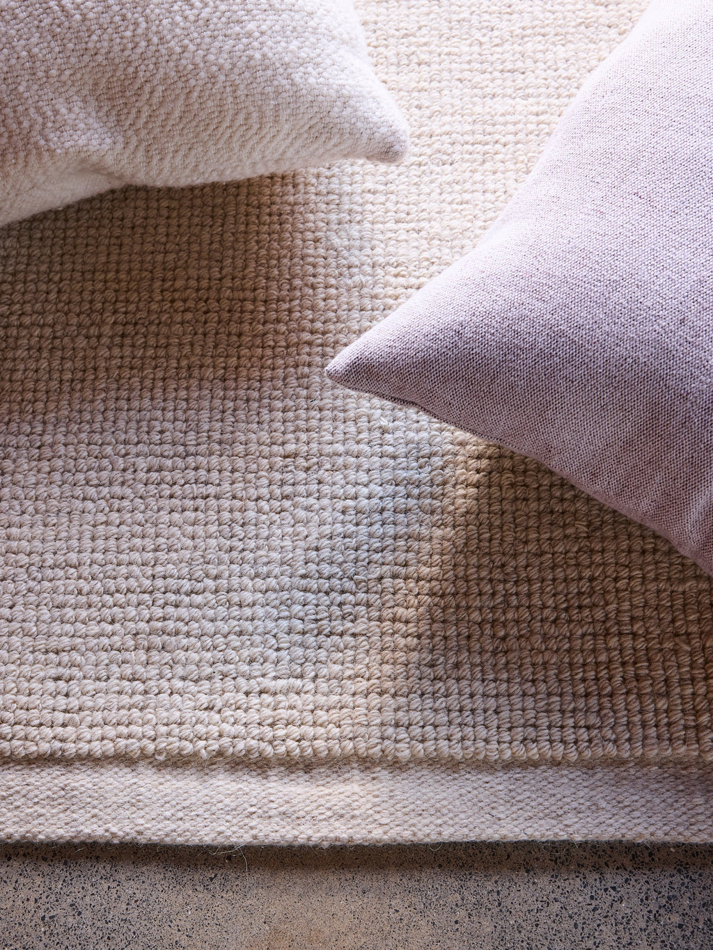 Città Joni Wool Mat in Oatmeal, close view styled with cushions in a living space.