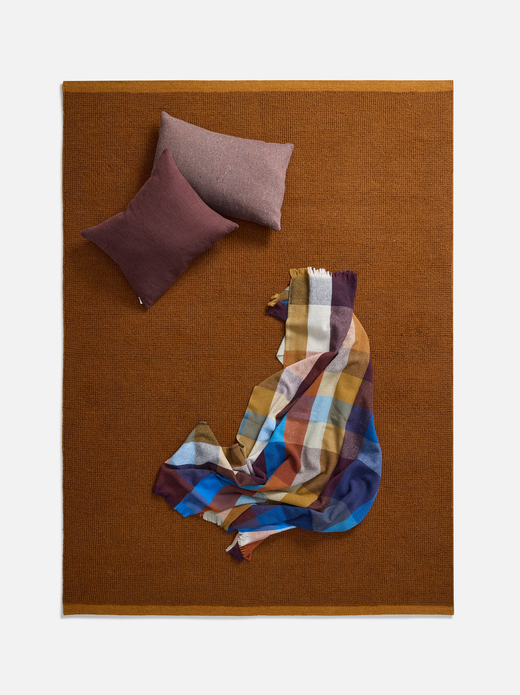 Città Joni Wool Mat in Orange Peel/Saffron, overhead view styled with cushions and a throw.