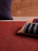 Città Joni Wool Mat in Paprika/Mulberry, close view styled with cushions in a living space.