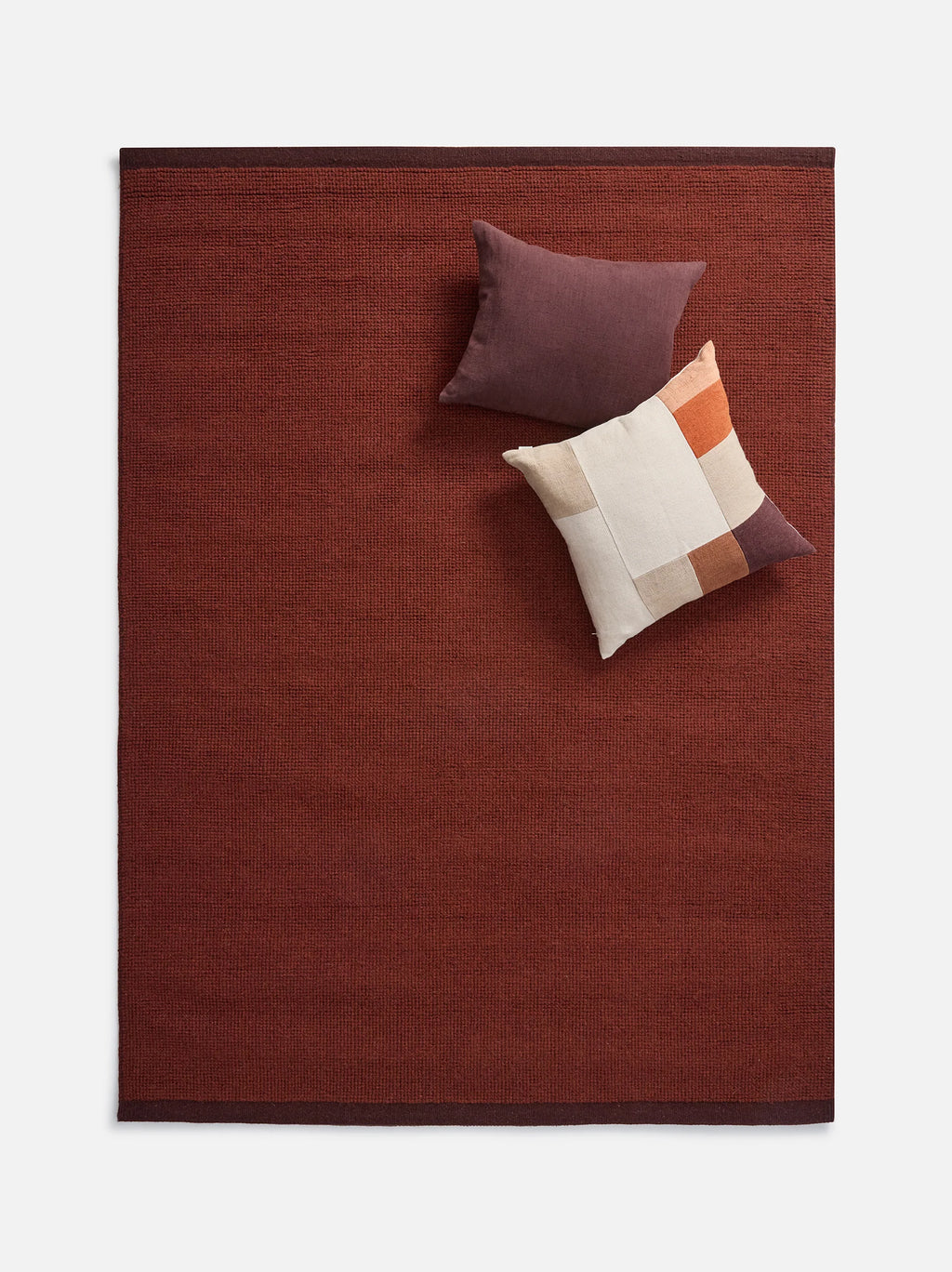 Città Joni Wool Mat in Paprika/Mulberry, overhead view styled with cushions.