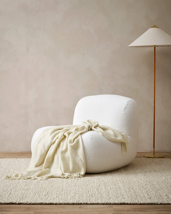 Soft, wool-blend creamy ecru coloured throw blanket draped over a chair in a contemporary living room