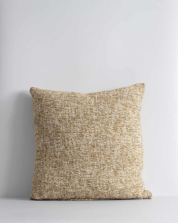 A textural woven cushion in shades of muted mustard yellow and ercu, by Baya