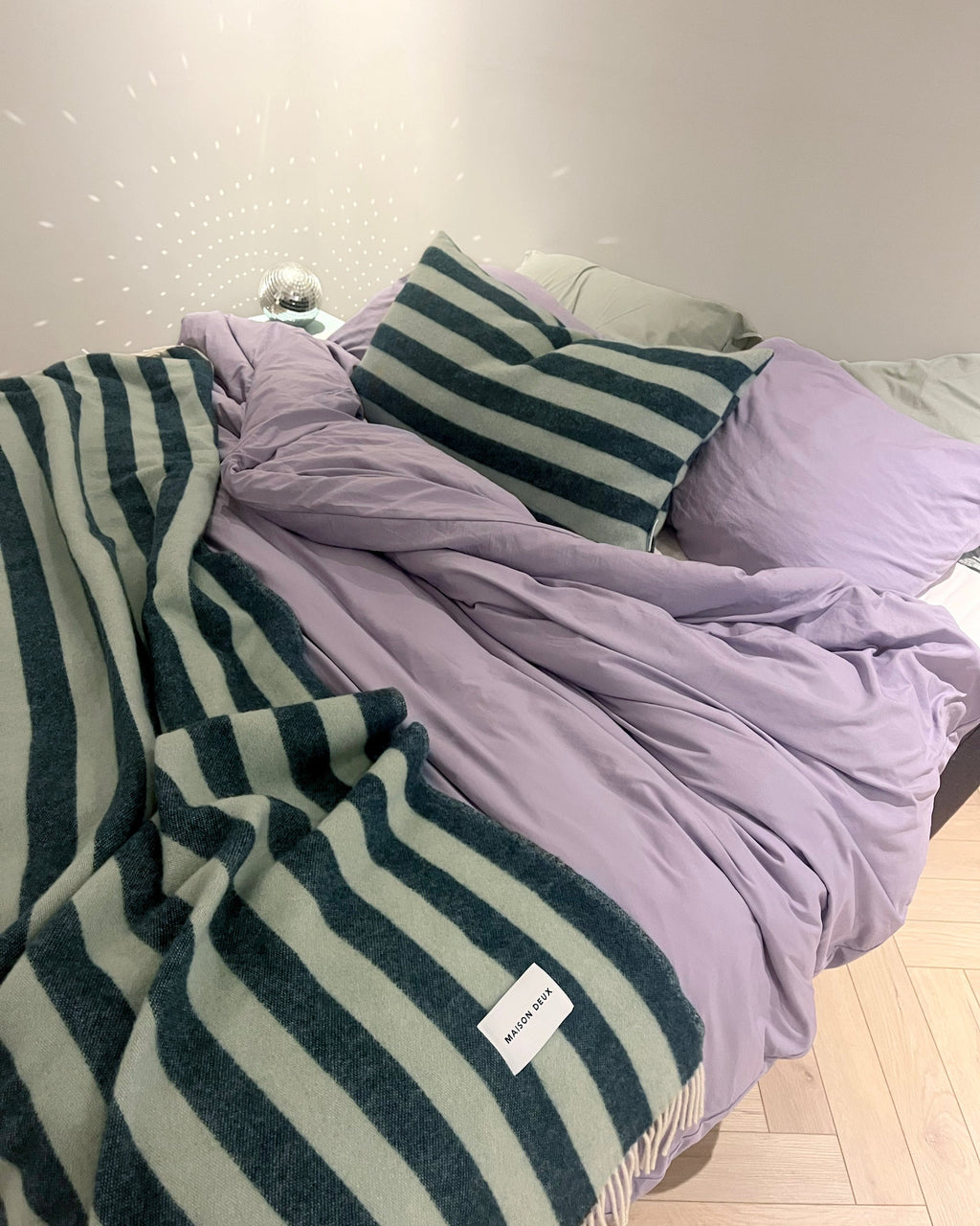 A stylish, cosy looking bed, with Maison Deux Candy Stripe throw blanket and pillow in sage green 