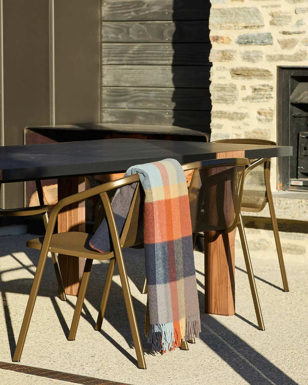 A multicoloured check throw in shades of orange, blue, and beige, draped over the back of a chair. 