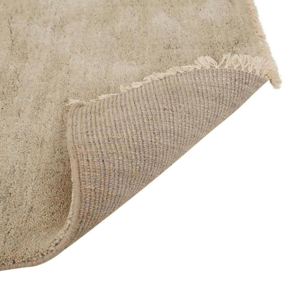 Corner of a soft handloomed rug in a soft beige Pumice colour by Soren Liv. The edges are lightly fringed, and flipped up to show the back of the rug