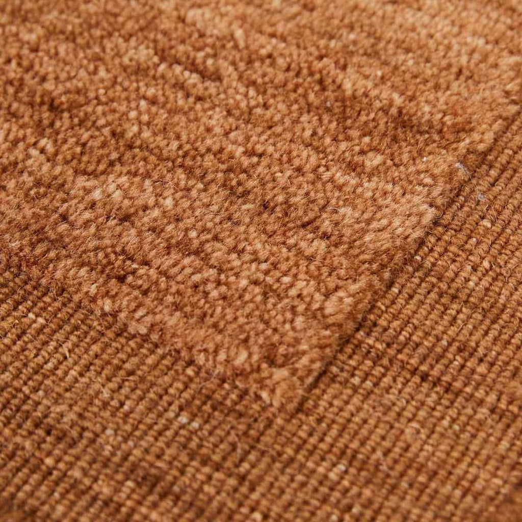 A close up of a handmade 100% wool rug by Globe West and Soren Liv NZ in a rich rust brown colour, with an indented border adding interest. 
