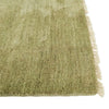 Corner image of a soft leaf-green handloomed woolen rug by Soren Liv. The edges are fringed with wool in a creamy ivory. 