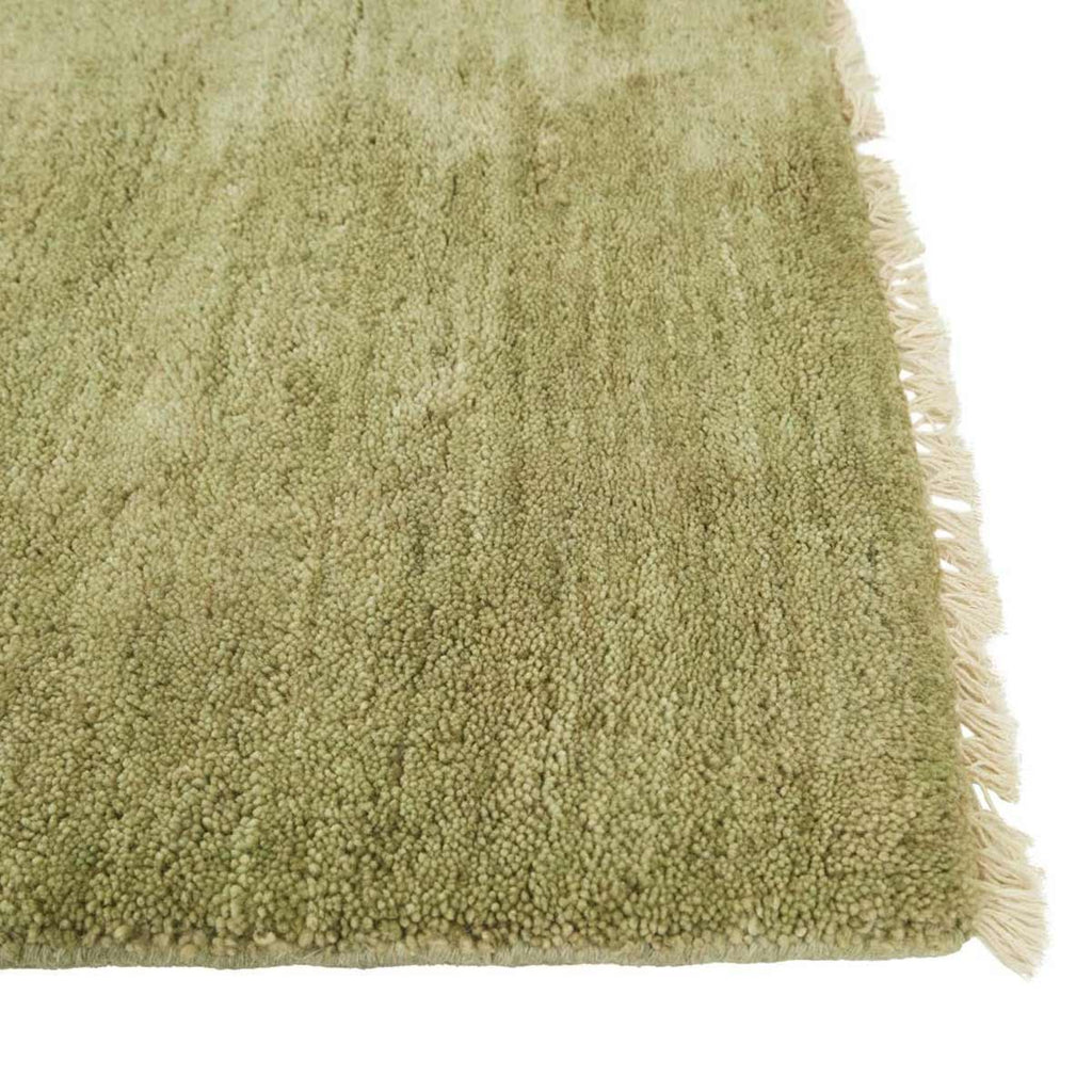 Corner image of a soft leaf-green handloomed woolen rug by Soren Liv. The edges are fringed with wool in a creamy ivory. 