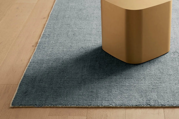 An ocean green contemporary floor rug in a wool blend, seen under a plinth on wooden floors