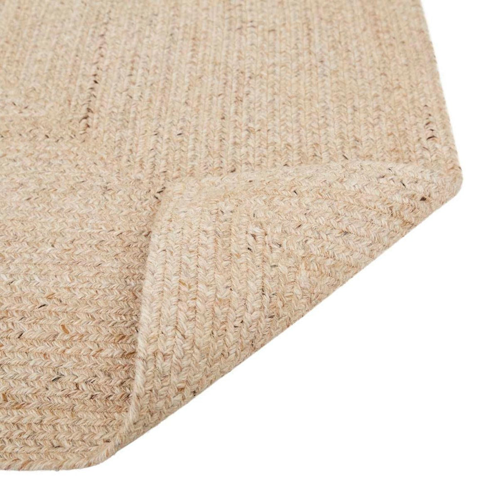 A corner view of a braided rug by Globe West and Soren Liv NZ in natural beige tones, perfect for outdoors or transition spaces. The edge of the rug is flipped up to reveal the underneath