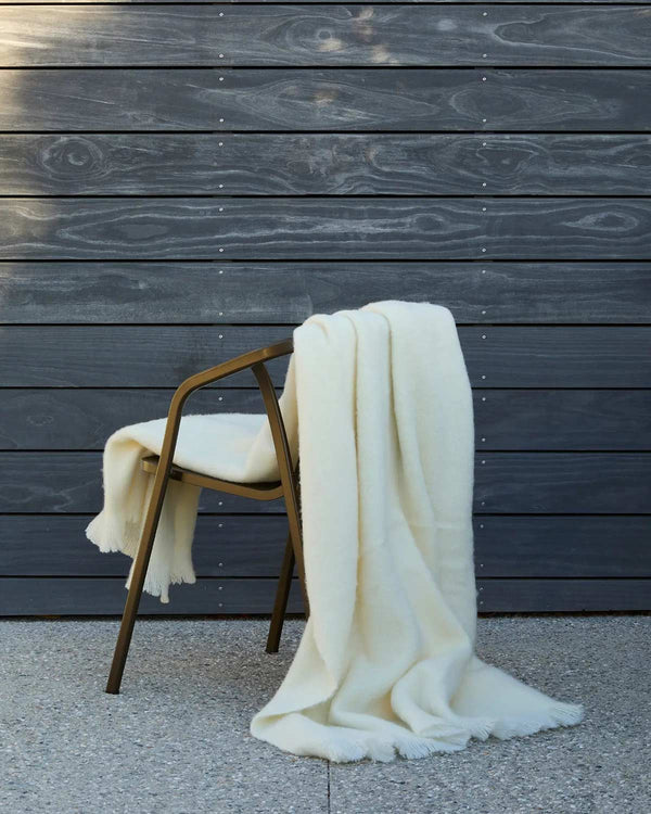 A soft warm cream toned wool throw blanket draped over a chair. 