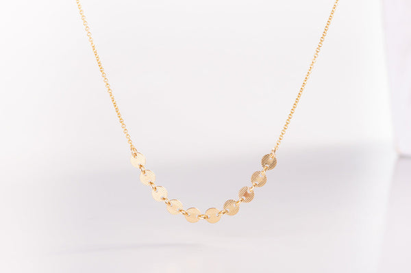 A close up view of the Italy necklace by Zoaje. Ten brushed metal gold-filled discs lie along the middle of the necklace. 