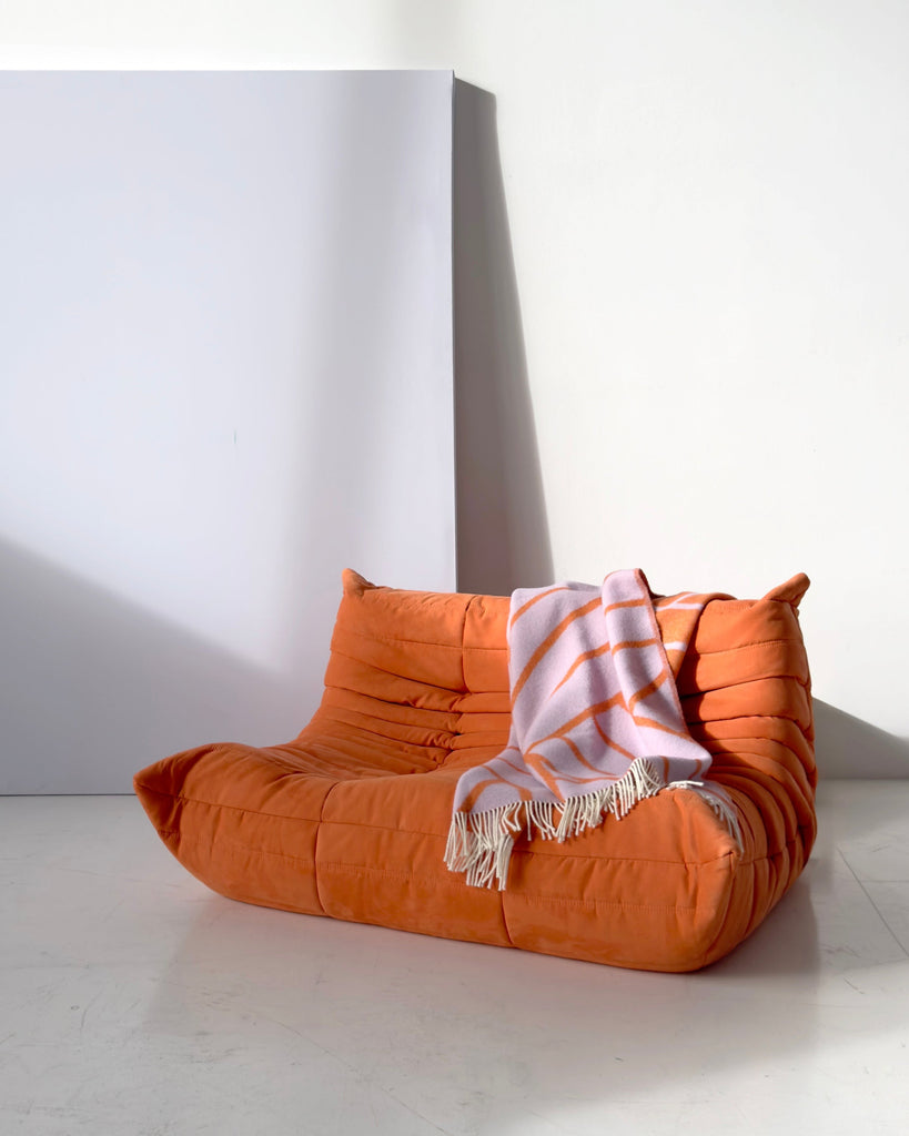 The Maison Deux throw blanket in pattern line, in shades of purple and orange, draped over a modern statement sofa