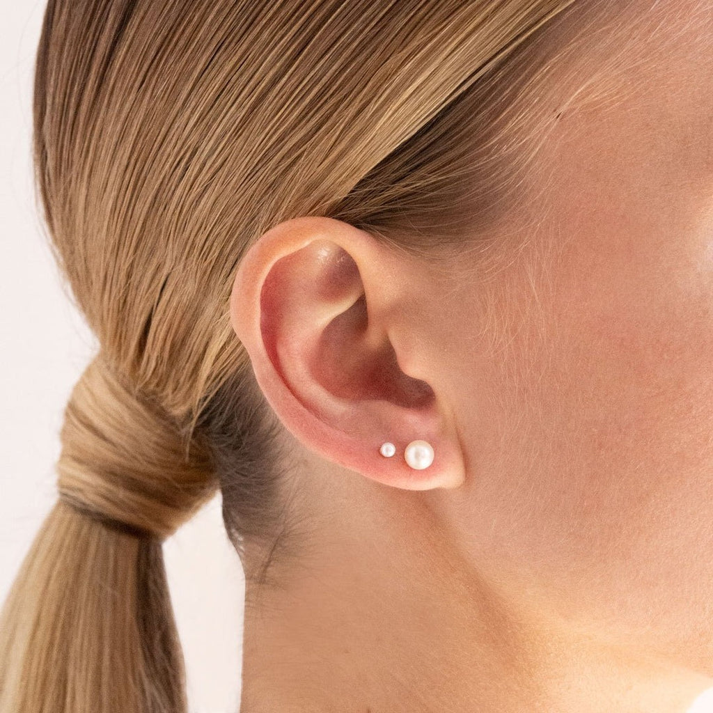 A woman wearing two differently sized pearl stud earrings. 