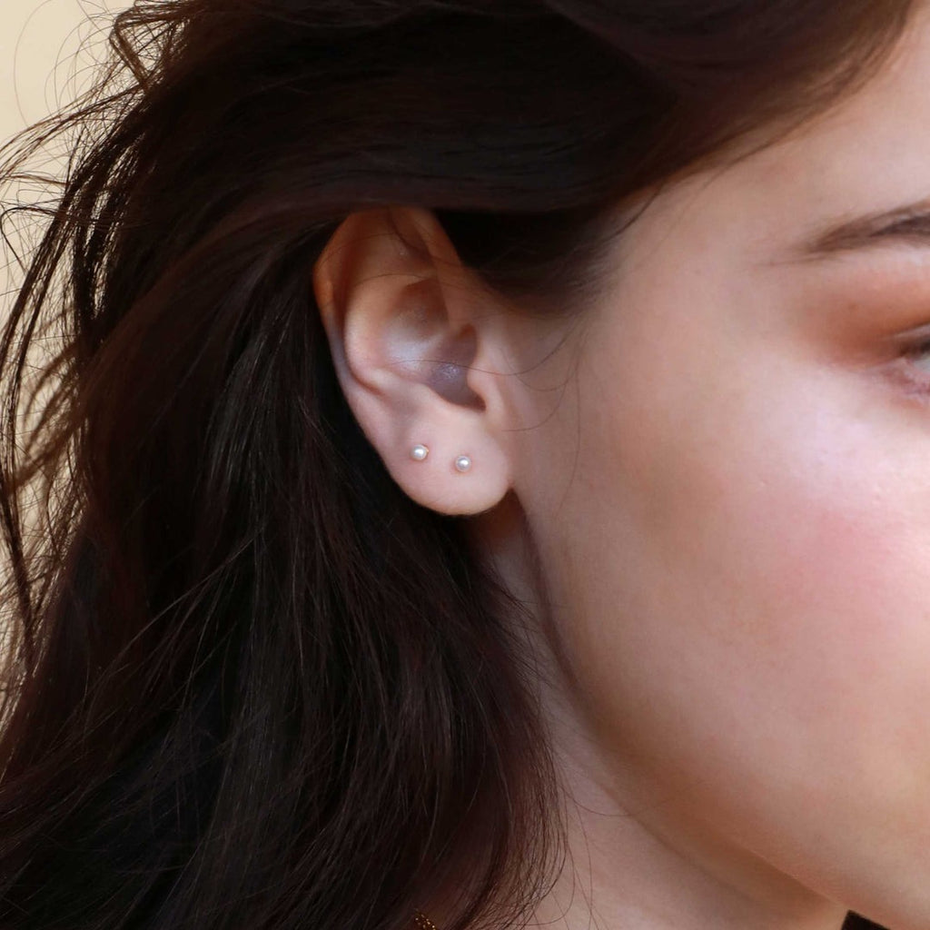 A woman wearing two dainty mini-pearl stud earrings. 