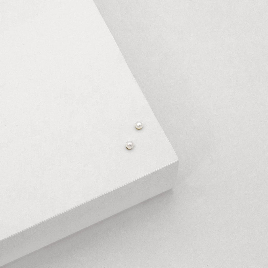 Two tiny delicate pearl stud earrings viewed from above. 