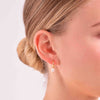 A woman wearing a delicate and simple pearl drop earring with a yellow gold hoop. 