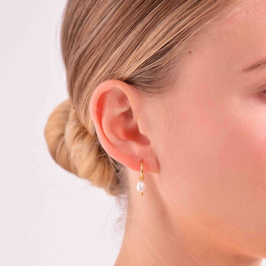 A woman wearing a delicate and simple pearl drop earring with a yellow gold hoop. 