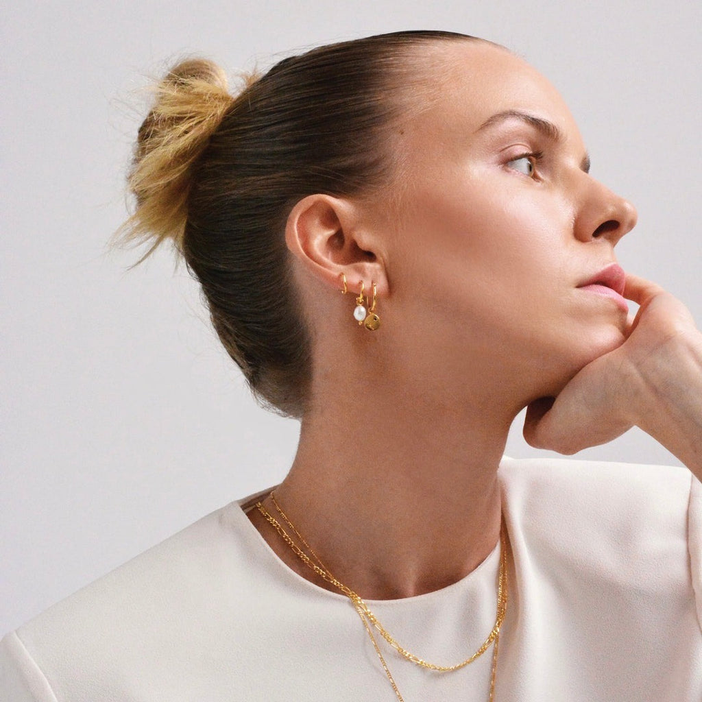 A woman wearing a stack of yellow gold plated earrings by Linda Tahija, one of which has a beautiful delicate freshwater pearl drop. 