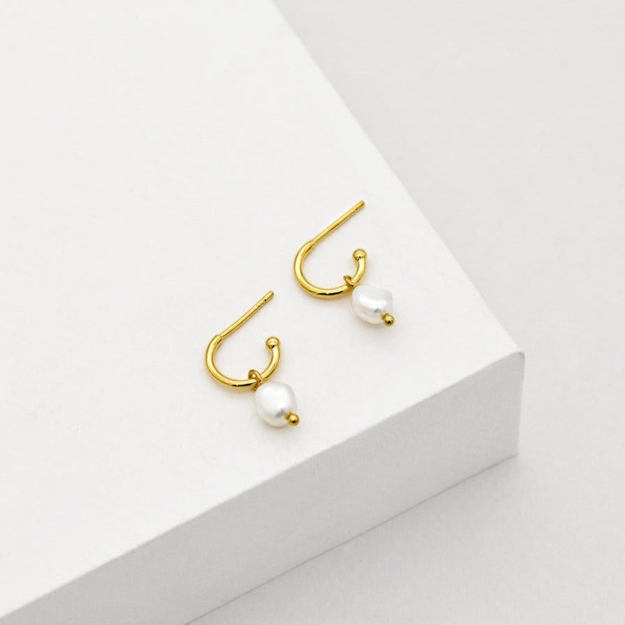 A pair of gold hoop earrings with freshwater pearl charms. 