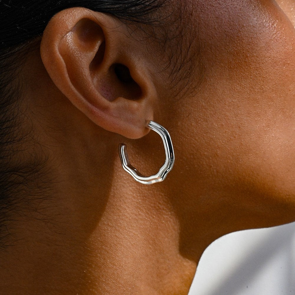 A woman wearing a chunky silver hoop earring with sculptural details. 
