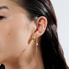 A woman wearing a statement stacked earring pairing with a chunky gold huggie hoop and a chain drop pearl. 