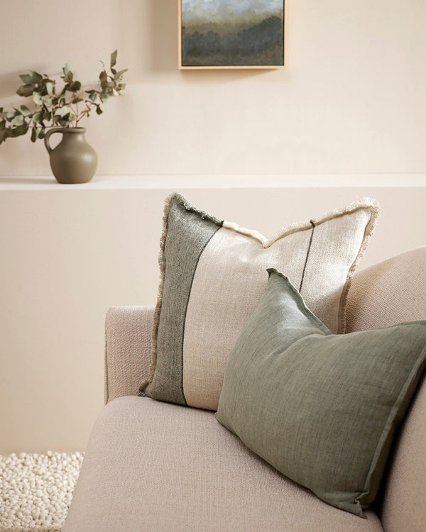 A natural linen cushion with sage green stripe and fringed edge detail, seen on a couch with a complementary green cushion