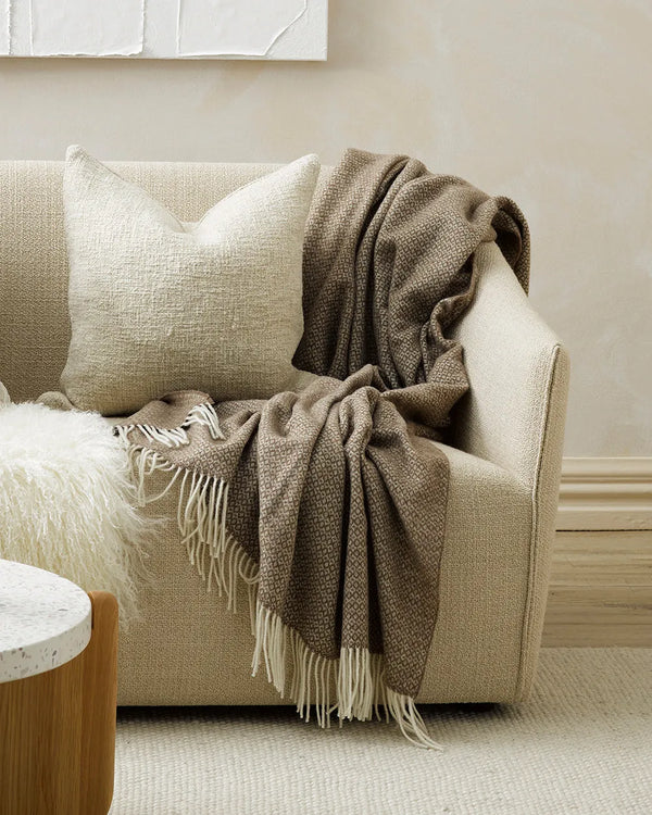 A soft brown, wool throw blanket by Baya, draped over the end of a couch
