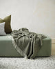 A soft, kahki green 'kale' throw blanket, with fringe, draped over an ottoman