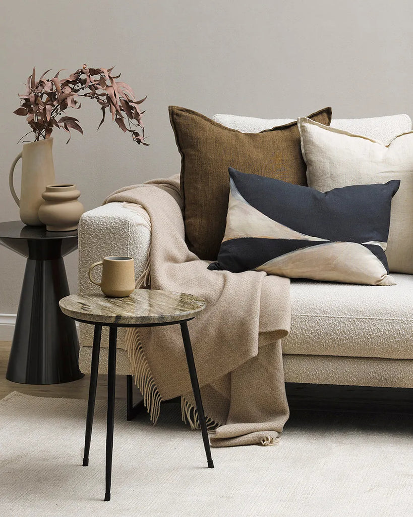 The Baya wool throw blanket 'Littano' in coloour cream oatmeal - draped over a couch and accessorised with Baya cushions