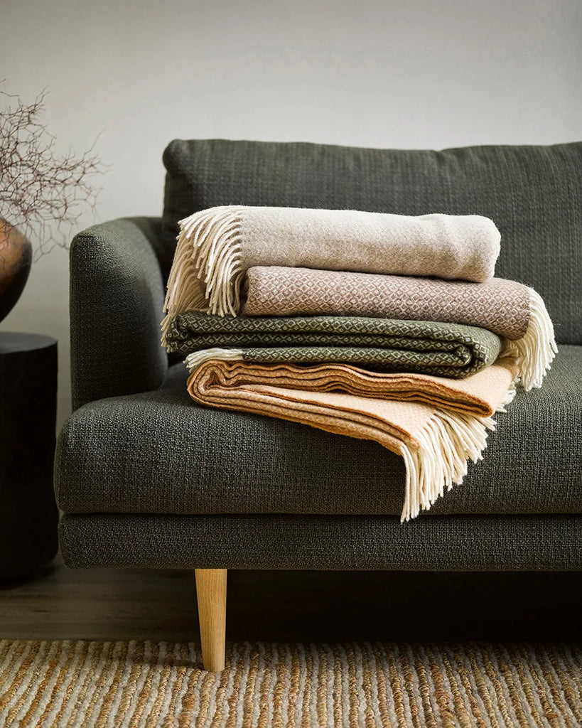 A stack of Baya Littano wool throws on a couch in a modern living room