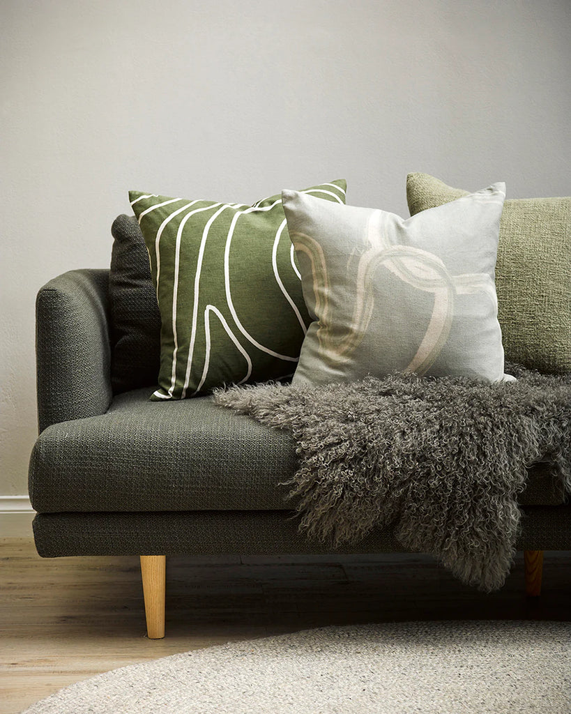 A couch in a modern living room, featuring three designer cushions by Baya