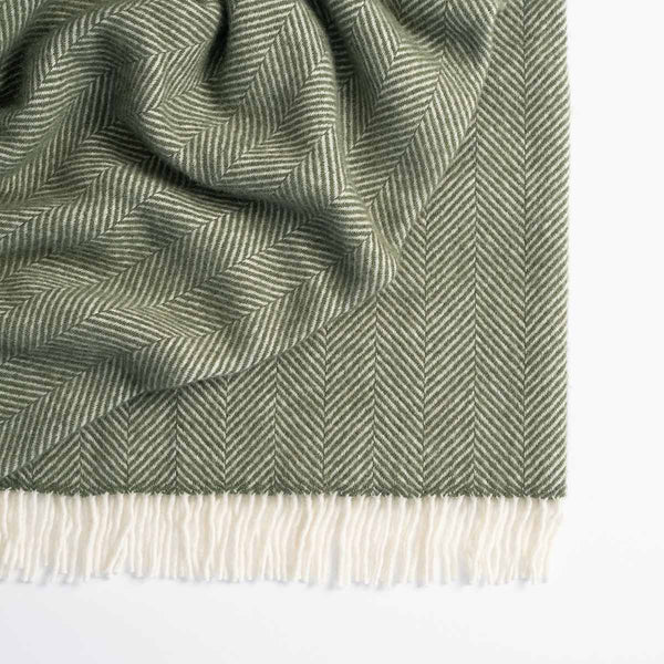 A trendy olive green and white herringbone patterned throw by Weave Home, with white fringed edging. 