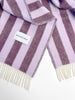 Maison Deux Candy Wrap wool throw in Lilac Aubergine, folded to show the woven brand label and fringe.