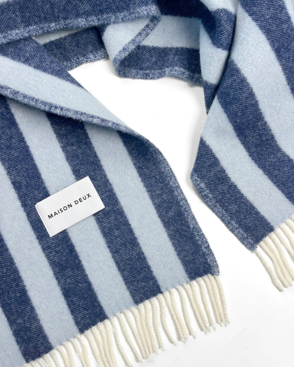 Maison Deux Candy Wrap wool throw in Navy Ice Blue, folded to show the woven brand label and the cream fringe