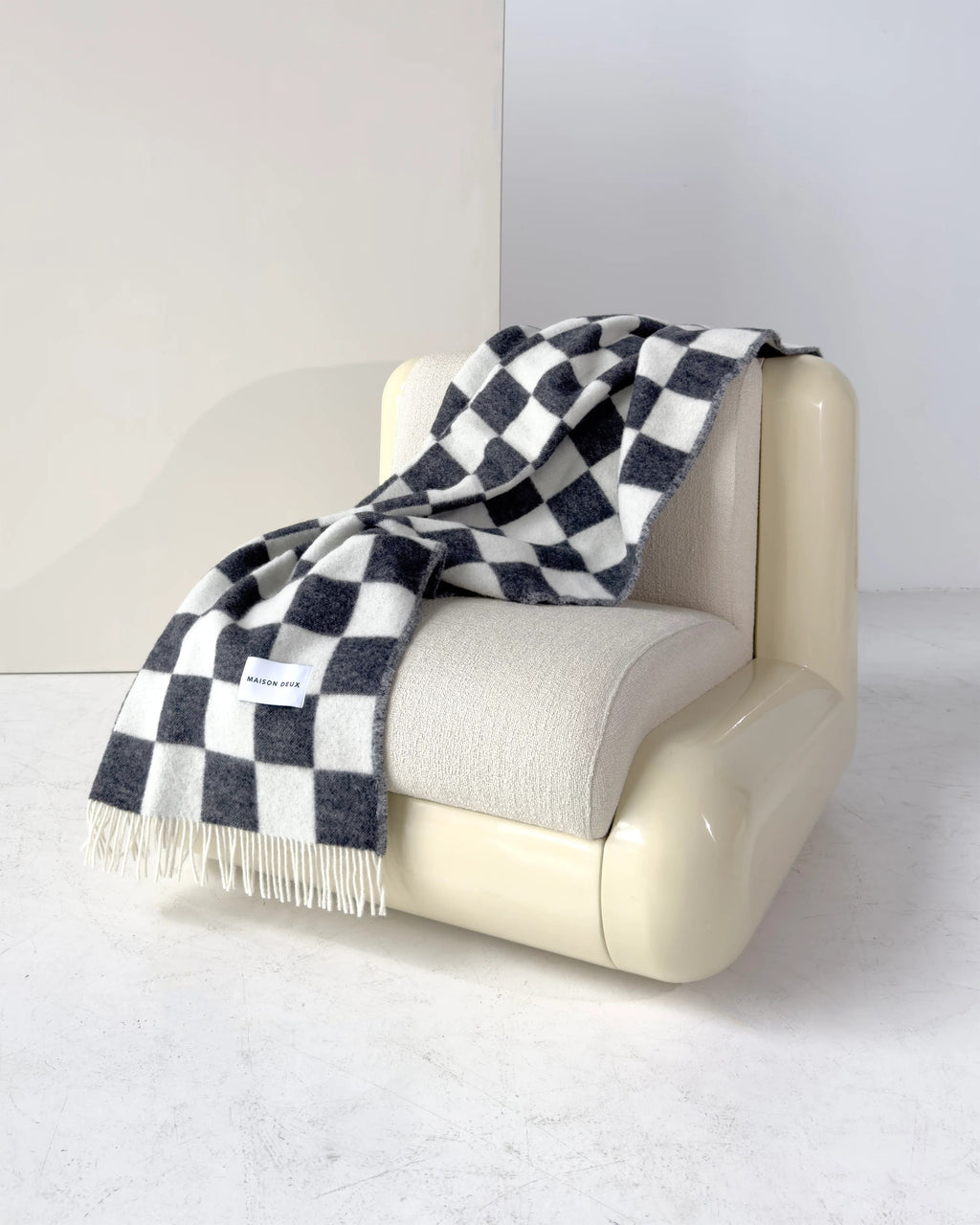 Maison Deux Checkerboard wool throw in Black White, draped over an armchair.