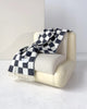 Maison Deux Checkerboard wool throw in Black White, draped over an armchair.