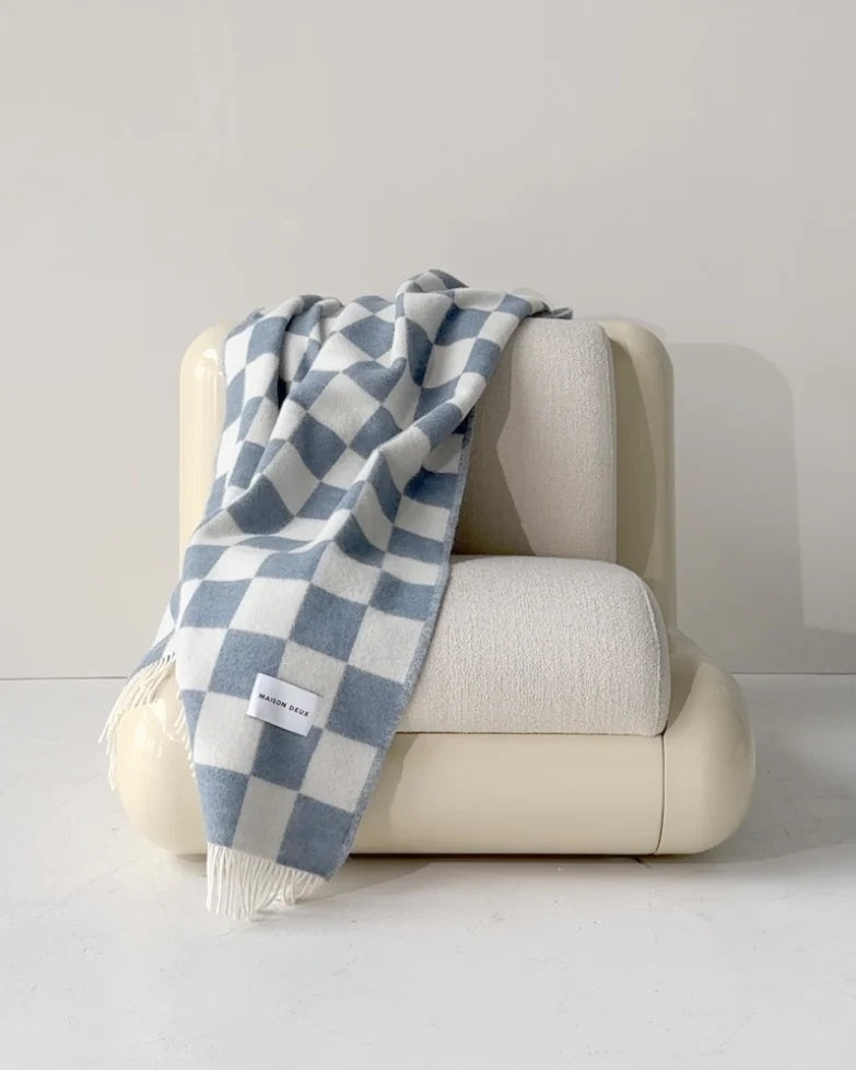 Maison Deux Checkerboard wool throw in Denim White, draped over an armchair.