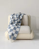 Maison Deux Checkerboard wool throw in Denim White, draped over an armchair.