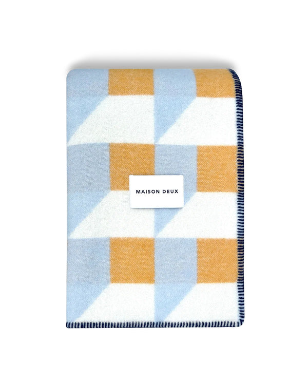 Maison Deux Cubics wool throw in Blue Honey, folded to show the cube pattern and the woven Maison Deux label