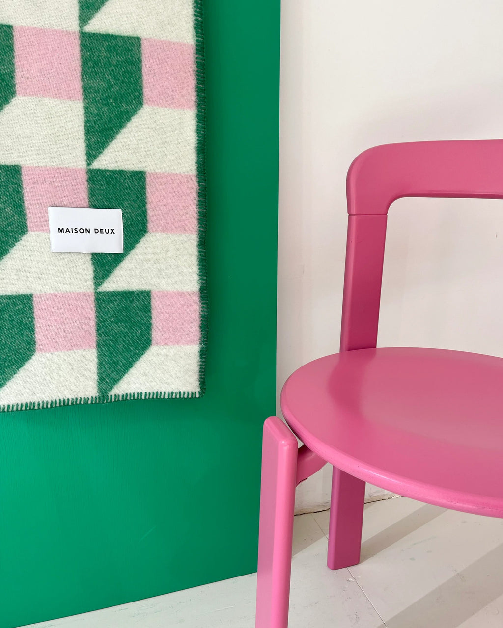 Maison Deux Cubics wool throw in Grass Pink, draped beside a pink chair against a green wall