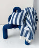 A modern designer blue chair with a matching cushion and throw blanket on it, both striped in shades of navy and light blue. 