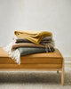 A stack of Baya Littano wool throw blankets on a stylish bench seat