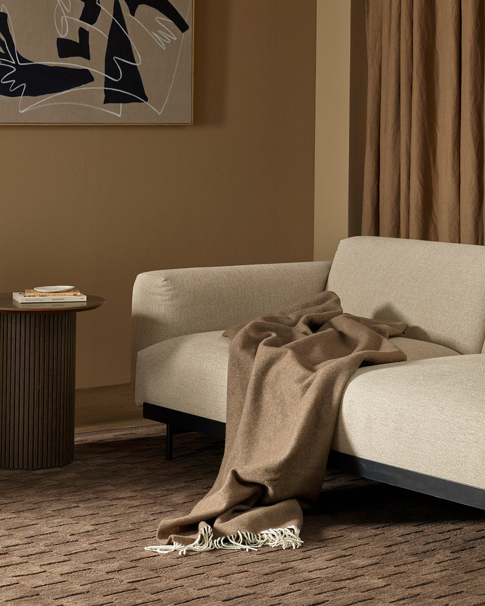 Beige sofa with a brown wool blanket draped over it in a room with a textural brown rug