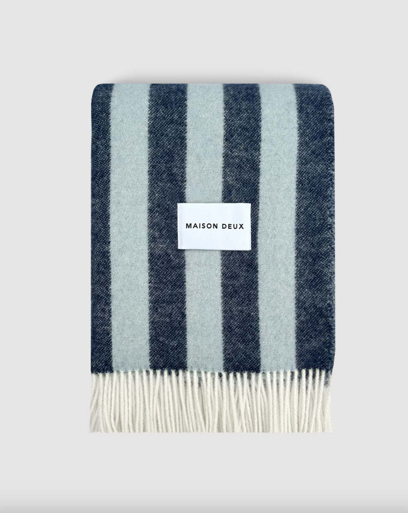 A folded large wool throw with navy and ice blue stripes, with a cream fringed edge. 