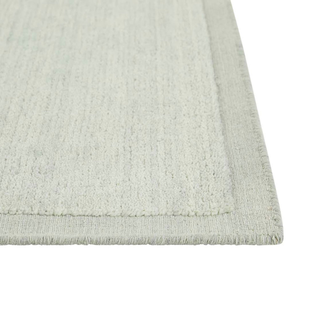 Close up of the corner of a handmade, 100% wool floor rug by Soren Liv NZ and Globe West, in subtle shades of light blue and green, shades of seafoam. The edges of the rug are indented, lending subtle sophistication.