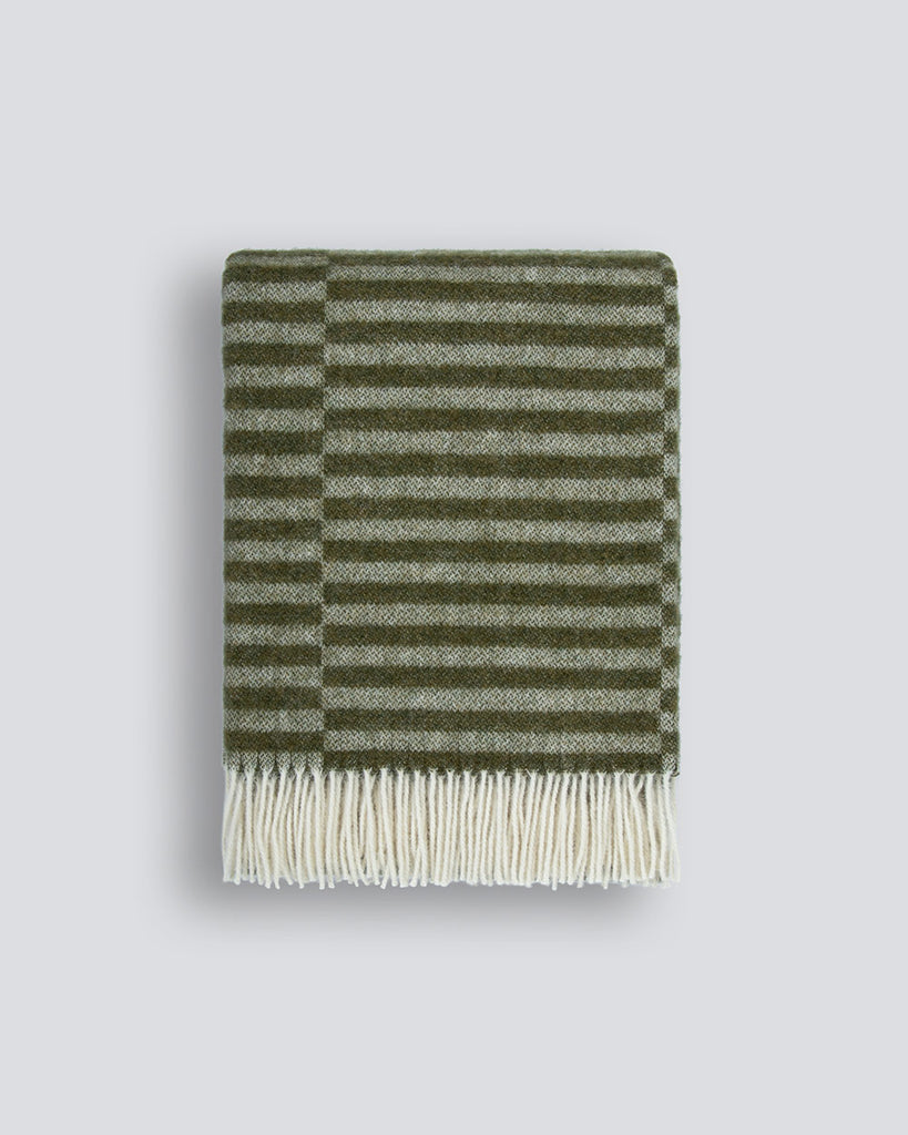 An off-set striped patterned throw blanket in shades of soft sage-green and olive, with a twisted fringe edge in 100% NZ wool by Baya