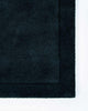 The corner of the Norfolk floor rug in the shade Ink. The border of the rug is cut-pile in a minimalist and refined design. 
