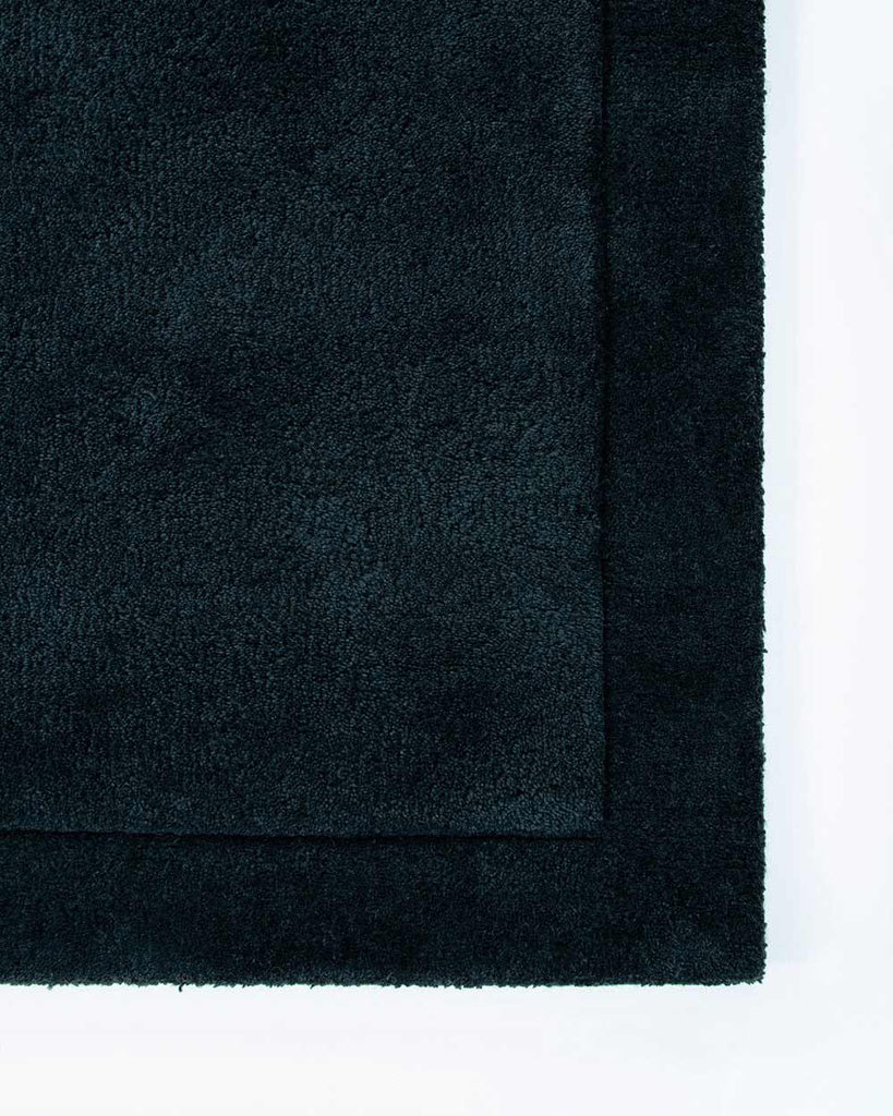 The corner of the Norfolk floor rug in the shade Ink. The border of the rug is cut-pile in a minimalist and refined design. 
